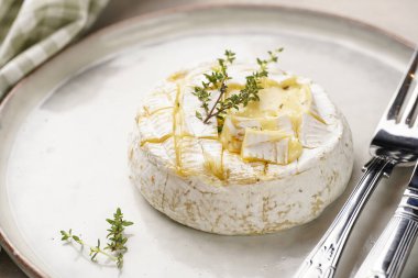 Beyaz tabakta fırında peynirli camembert peyniri, gri beton yüzey. Kekikli ev yapımı ızgara peynir, tarama stili masa seti.