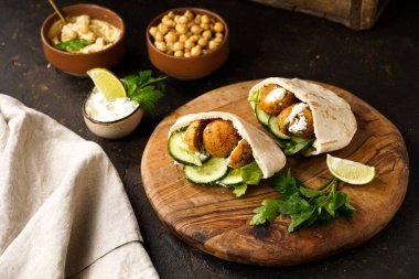 Geleneksel oryantal nohut köftesi pide, tzatziki yoğurt sosu, humus, ahşap tahtada taze limon ve yeşil kişniş, koyu yüzey.