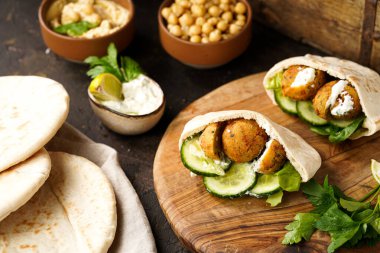 Geleneksel oryantal nohut köftesi pide, tzatziki yoğurt sosu, humus, ahşap tahtada taze limon ve yeşil kişniş, koyu yüzey.