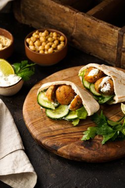 Geleneksel oryantal nohut köftesi pide, tzatziki yoğurt sosu, humus, ahşap tahtada taze limon ve yeşil kişniş, koyu yüzey.