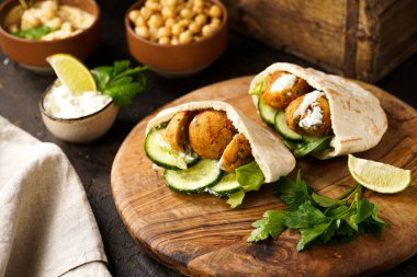 Geleneksel oryantal nohut köftesi pide, tzatziki yoğurt sosu, humus, ahşap tahtada taze limon ve yeşil kişniş, koyu yüzey.