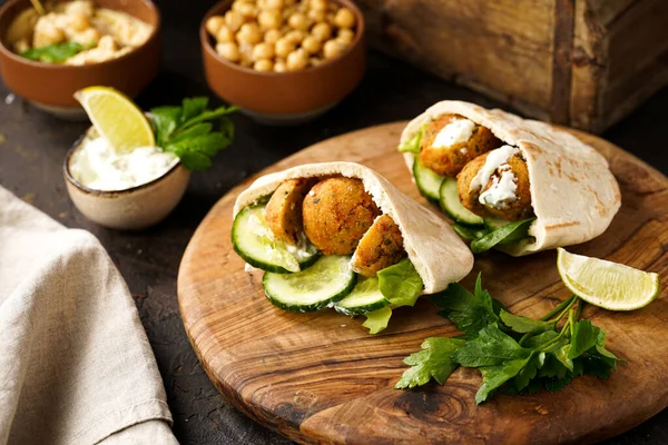 Geleneksel oryantal nohut köftesi pide, tzatziki yoğurt sosu, humus, ahşap tahtada taze limon ve yeşil kişniş, koyu yüzey.