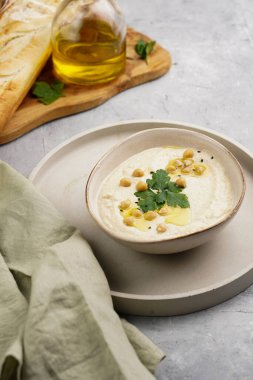 Nohut soslu humus ve maydanozlu seramik kase beton yüzeyde kızarmış baget dilimleri ve ahşap tahtada zeytinyağı.