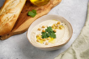 Nohut soslu humus ve maydanozlu seramik kase beton yüzeyde kızarmış baget dilimleri ve ahşap tahtada zeytinyağı.