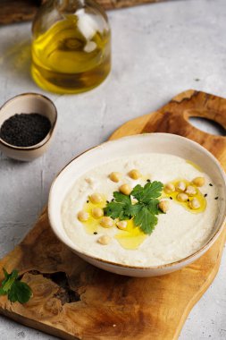 Nohut soslu humus ve maydanozlu seramik kase beton yüzeyde kızarmış baget dilimleri ve ahşap tahtada zeytinyağı.