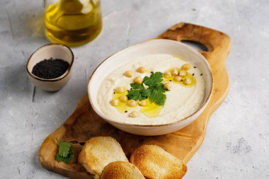 Nohut soslu humus ve maydanozlu seramik kase beton yüzeyde kızarmış baget dilimleri ve ahşap tahtada zeytinyağı.