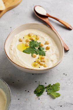 Nohut soslu humus ve maydanozlu seramik kase beton yüzeyde kızarmış baget dilimleri ve ahşap tahtada zeytinyağı.