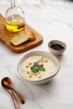 Nohut soslu humus ve maydanozlu seramik kasede mermer yüzeyde kızarmış baget dilimleri ve ahşap tahtada zeytinyağı.