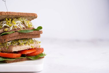 Lezzetli vejetaryen sandviçler, kahverengi protein ekmeği, tofu peyniri, domates, ıspanak ve mikroyeşillikler üst üste istiflenmiş, beyaz arka plan.