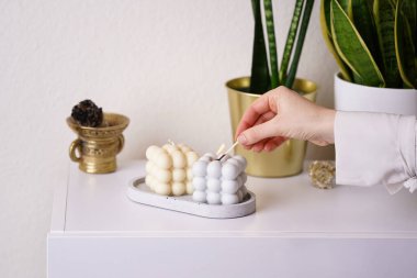 Beyaz büfedeki beton tepside gri ve beyaz baloncuk mumları yakan kadın el, sansevieria yeşil ev planları, leke çubuğu.