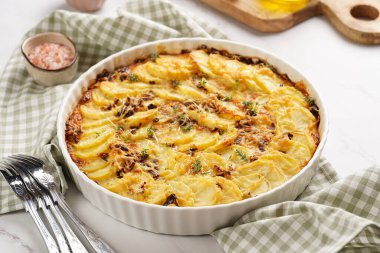 Kırmızı soğanlı patates güveci yeşil kareli mutfak havlusunda taze kekik ve biberiye aromalı ahşap tahta biber, tuz, zeytinyağı.
