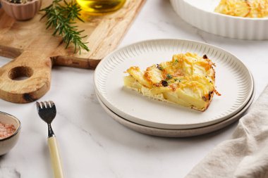 Kırmızı soğanlı patates güveci, yeşil kareli mutfak havlusunda taze kekik ve biberiye aromalı ahşap tahta: biber, tuz, zeytinyağı