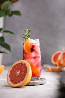 Greyfurtlu soğuk portakal suyu, donmuş böğürtlen ve buz küpleri, biberiye, yarım greyfurt ve gri arkaplan.