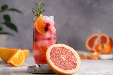 Greyfurtlu soğuk portakal suyu, donmuş böğürtlen ve buz küpleri, biberiye, yarım greyfurt ve gri arkaplan.
