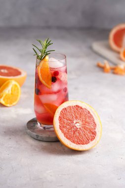 Greyfurtlu soğuk portakal suyu, donmuş böğürtlen ve buz küpleri, biberiye, yarım greyfurt ve gri arkaplan.