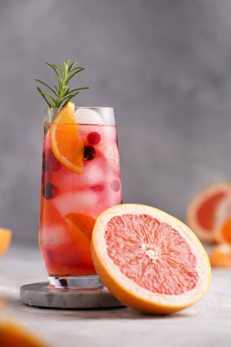 Greyfurtlu soğuk portakal suyu, donmuş böğürtlen ve buz küpleri, biberiye, yarım greyfurt ve gri arkaplan.