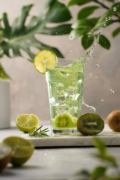 緑の植物の設定で大理石のボード上のスプラッシュと背の高い長いガラスでキウイ 石灰と氷のキューブと緑のさわやかな飲み物 — ストック写真