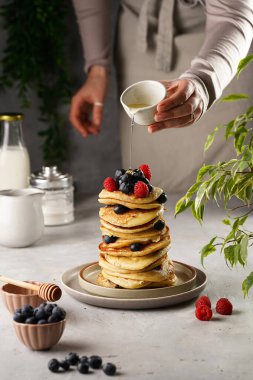 Geleneksel böğürtlen kreplerinin üzerine ballı akçaağaç pekmezi döken bir kadın ve üst üste ahududu ve ceviz.