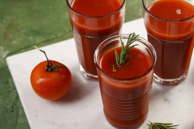 Kırmızı alkolsüz domates suyuyla dolu birkaç bardak yeşil arka planda mermer tabakta.