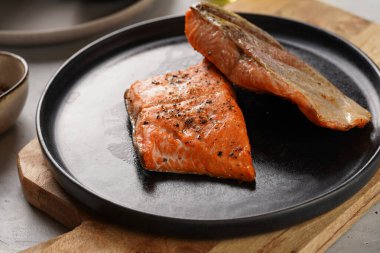 İki ızgara balık bifteği. Tahta tahtada siyah yuvarlak tabakta kırmızı somon, zeytinyağı, gri arka planda avokado.