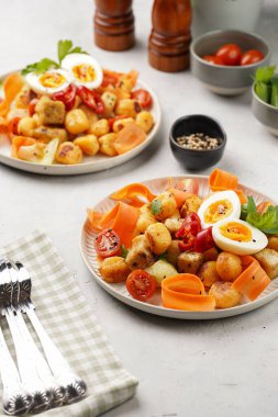 Tatlı patates gnocchi ve teriyaki tofu ile Endonezya sebze salatası gado - havuç, salatalık, domates, kişniş, susam tohumu, haşlanmış yumurta ve fıstık ezmesi sosu beyaz tabakta.