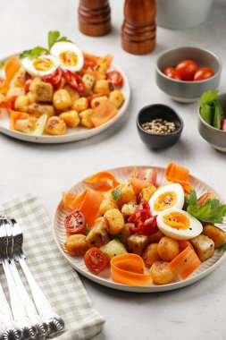 Tatlı patates gnocchi ve teriyaki tofu ile Endonezya sebze salatası gado - havuç, salatalık, domates, kişniş, susam tohumu, haşlanmış yumurta ve fıstık ezmesi sosu beyaz tabakta.