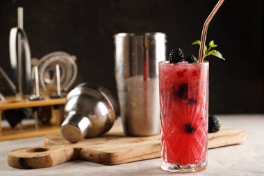 Klasik böğürtlen ve cin kokteylinin alkolsüz mocktail versiyonu olan uzun bir bardak. Tahta üzerinde böğürtlen, kokteyl ekipmanı.