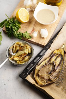 Geleneksel Arap mutfağı bej ganoush yemeği için malzemeler: kase, tahin, kişniş, sarımsak, zeytinyağı, ahşap tahtada limon suyu ve pişirme tepsisinde kızartılmış patlıcan.