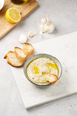 Geleneksel Arap mutfağı baba ganoush kızarmış patlıcan, tahin, kişniş, sarımsak, zeytin yağı, limon suyu, kızarmış baget ekmek ve gri arka planda beyaz mermer tahta.