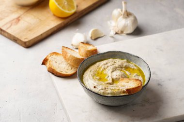 Geleneksel Arap mutfağı baba ganoush kızarmış patlıcan, tahin, kişniş, sarımsak, zeytin yağı, limon suyu, kızarmış baget ekmek ve gri arka planda beyaz mermer tahta.