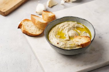 Geleneksel Arap mutfağı baba ganoush kızarmış patlıcan, tahin, kişniş, sarımsak, zeytin yağı, limon suyu, kızarmış baget ekmek ve gri arka planda beyaz mermer tahta.