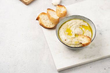 Geleneksel Arap mutfağı baba ganoush kızarmış patlıcan, tahin, kişniş, sarımsak, zeytin yağı, limon suyu, kızarmış baget ekmek ve gri arka planda beyaz mermer tahta.