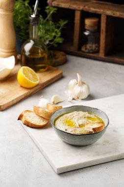 Geleneksel Arap mutfağı baba ganoush kızarmış patlıcan, tahin, kişniş, sarımsak, zeytin yağı, limon suyu, kızarmış baget ekmek ve gri arka planda beyaz mermer tahta.