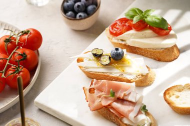 İtalyan antipasto bruschetta - füme jambon, keçi peyniri, yabanmersini, mozzarella, domates, mermer tahtada fesleğen, limonlu su bardağı ile beyaz ekmek dilimleri