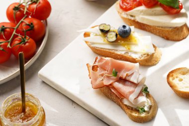 İtalyan antipasto bruschetta - füme jambon, keçi peyniri, yabanmersini, mozzarella, domates, mermer tahtada fesleğen, limonlu su bardağı ile beyaz ekmek dilimleri