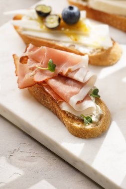 İtalyan antipasto bruschetta - füme jambon, keçi peyniri, yabanmersini, mozzarella, domates, mermer tahtada fesleğen, limonlu su bardağı ile beyaz ekmek dilimleri