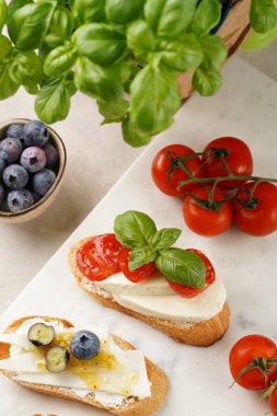 İtalyan antipasto bruschetta - füme jambon, keçi peyniri, yabanmersini, mozzarella, domates, mermer tahtada fesleğen, limonlu su bardağı ile beyaz ekmek dilimleri