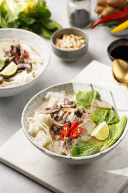 Pho Bo Vietnam çorbası sığır eti, pirinç eriştesi, pak choi ve mantarlar mermer tahtada gri bir kasede, fıstık, soya sosu, kırmızı biber