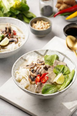 Pho Bo Vietnam çorbası sığır eti, pirinç eriştesi, pak choi ve mantarlar mermer tahtada gri bir kasede, fıstık, soya sosu, kırmızı biber