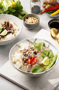 Pho Bo Vietnam çorbası sığır eti, pirinç eriştesi, pak choi ve mantarlar mermer tahtada gri bir kasede, fıstık, soya sosu, kırmızı biber