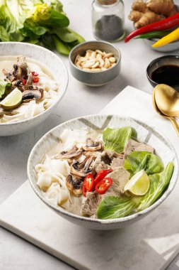 Pho Bo Vietnam çorbası sığır eti, pirinç eriştesi, pak choi ve mantarlar mermer tahtada gri bir kasede, fıstık, soya sosu, kırmızı biber