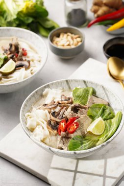 Pho Bo Vietnam çorbası sığır eti, pirinç eriştesi, pak choi ve mantarlar mermer tahtada gri bir kasede, fıstık, soya sosu, kırmızı biber