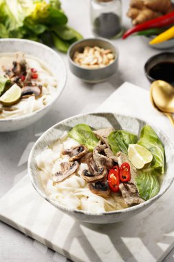 Pho Bo Vietnam çorbası sığır eti, pirinç eriştesi, pak choi ve mantarlar mermer tahtada gri bir kasede, fıstık, soya sosu, kırmızı biber