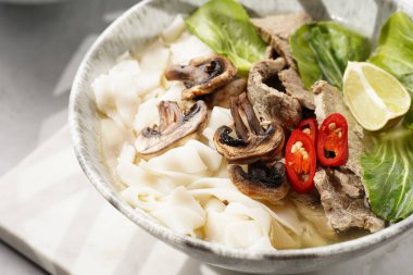 Pho Bo Vietnam çorbası sığır eti, pirinç eriştesi, pak choi ve mantarlar mermer tahtada gri bir kasede, fıstık, soya sosu, kırmızı biber