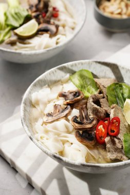 Pho Bo Vietnam çorbası sığır eti, pirinç eriştesi, pak choi ve mantarlar mermer tahtada gri bir kasede, fıstık, soya sosu, kırmızı biber
