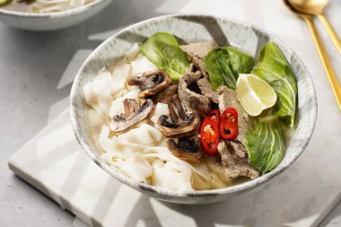 Pho Bo Vietnam çorbası sığır eti, pirinç eriştesi, pak choi ve mantarlar mermer tahtada gri bir kasede, fıstık, soya sosu, kırmızı biber