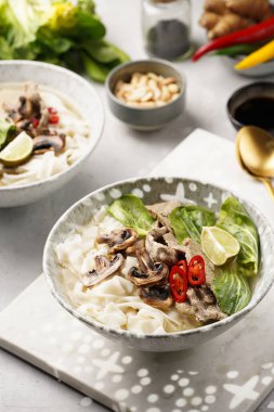 Pho Bo Vietnam çorbası sığır eti, pirinç eriştesi, pak choi ve mantarlar mermer tahtada gri bir kasede, fıstık, soya sosu, kırmızı biber