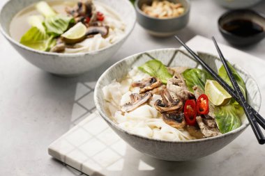 Pho Bo Vietnam çorbası sığır eti, pirinç eriştesi, pak choi ve mantarlar mermer tahtada gri bir kasede, fıstık, soya sosu, kırmızı biber