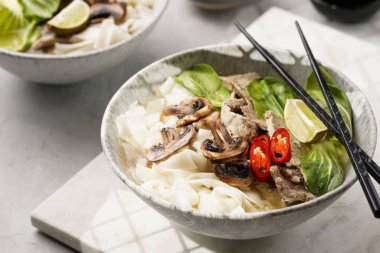 Pho Bo Vietnam çorbası sığır eti, pirinç eriştesi, pak choi ve mantarlar mermer tahtada gri bir kasede, fıstık, soya sosu, kırmızı biber