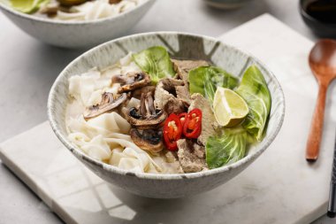 Pho Bo Vietnam çorbası sığır eti, pirinç eriştesi, pak choi ve mantarlar mermer tahtada gri bir kasede, fıstık, soya sosu, kırmızı biber